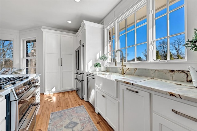 kitchen with high quality appliances, a sink, white cabinets, light wood finished floors, and light stone countertops