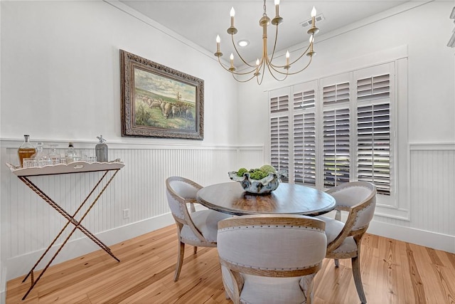 dining space with a wainscoted wall, a notable chandelier, wood finished floors, and visible vents