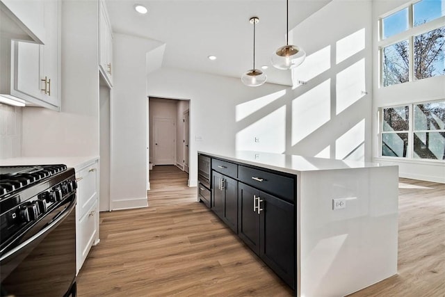 kitchen featuring light wood finished floors, dark cabinets, light countertops, and black gas stove