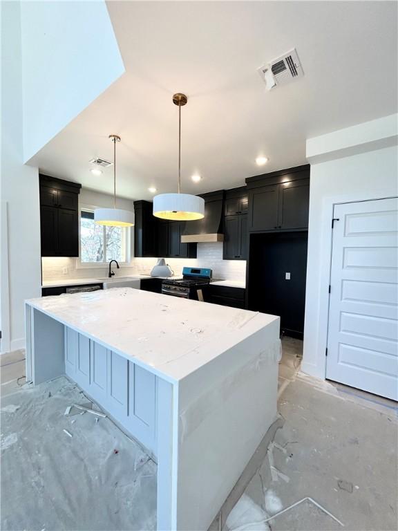 kitchen featuring visible vents, wall chimney range hood, decorative backsplash, dark cabinetry, and stainless steel gas stove