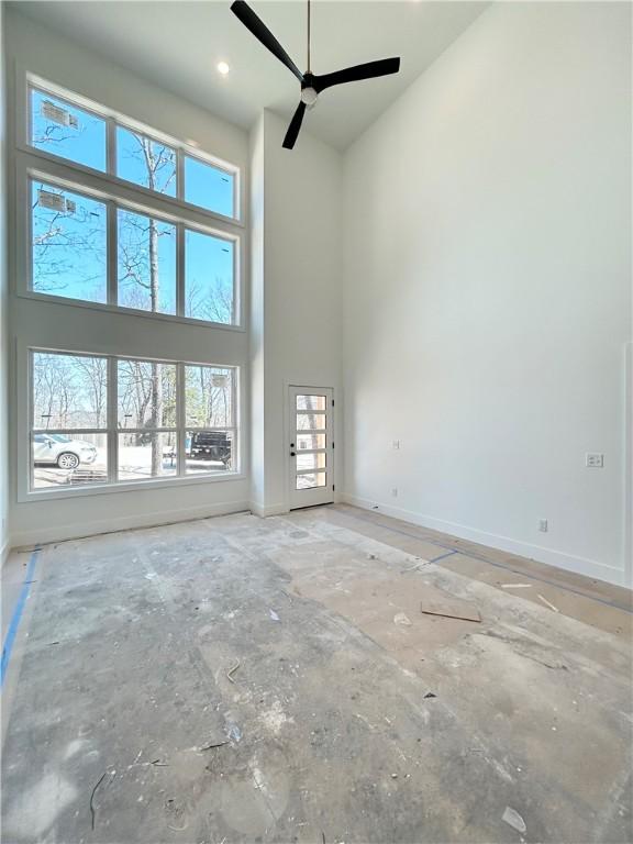 unfurnished living room featuring a ceiling fan, baseboards, and a towering ceiling