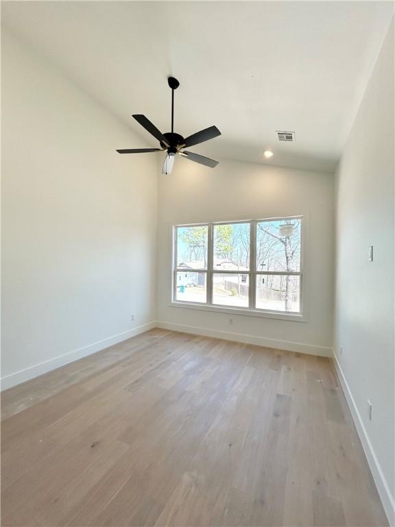 empty room featuring visible vents, light wood-type flooring, baseboards, and vaulted ceiling