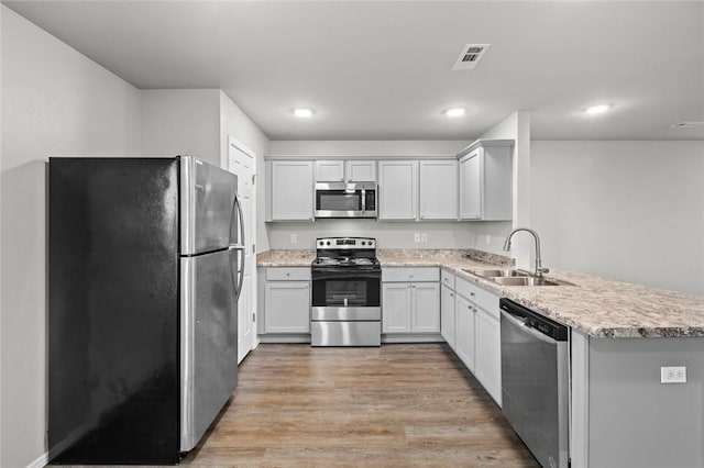 kitchen featuring visible vents, a peninsula, stainless steel appliances, light wood-style floors, and a sink