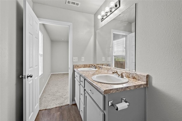 bathroom with double vanity, visible vents, a sink, and wood finished floors