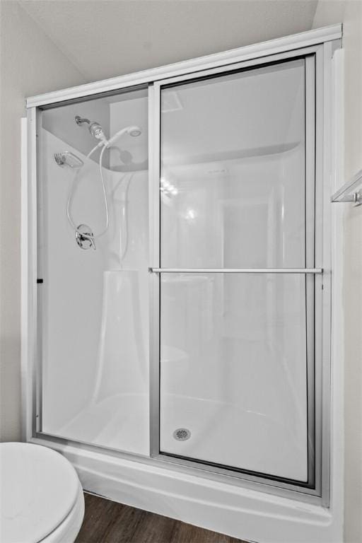 bathroom featuring toilet, a stall shower, and wood finished floors