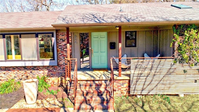 view of exterior entry with board and batten siding, a porch, brick siding, and a shingled roof