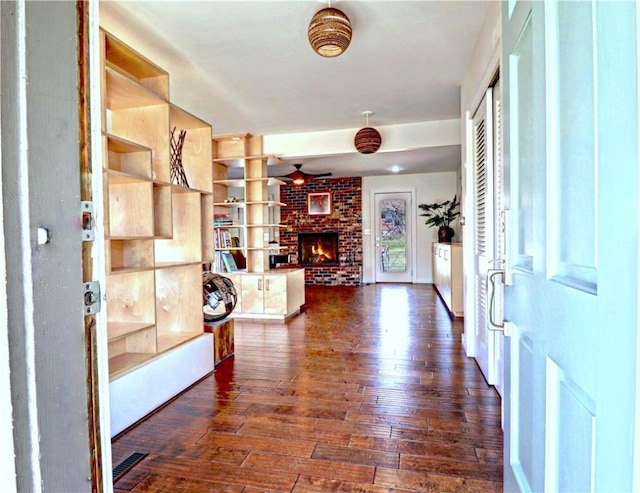 foyer featuring visible vents, a brick fireplace, ceiling fan, and dark wood-style flooring