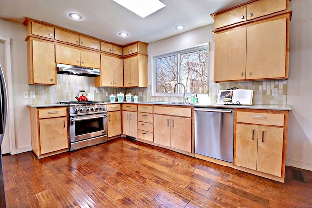 kitchen featuring light brown cabinetry, under cabinet range hood, a sink, stainless steel appliances, and dark wood-style flooring