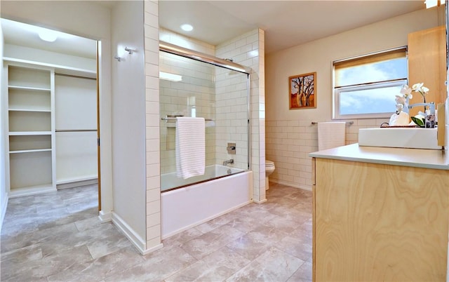 full bathroom with a walk in closet, toilet, combined bath / shower with glass door, tile walls, and vanity