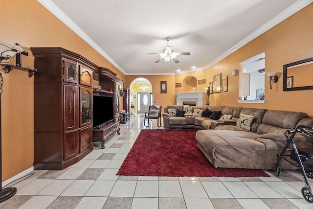 living area featuring light tile patterned floors, arched walkways, ceiling fan, ornamental molding, and a fireplace