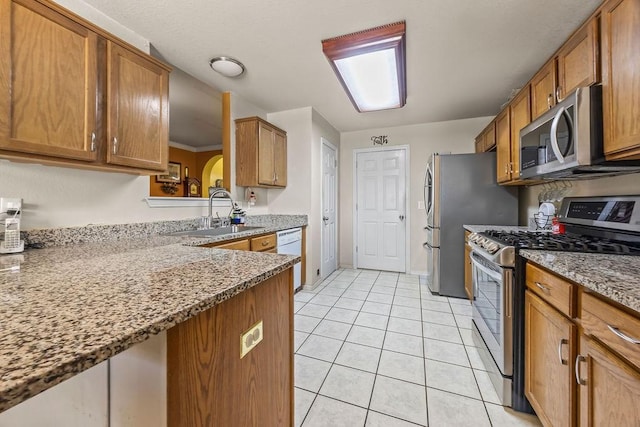 kitchen featuring stone countertops, appliances with stainless steel finishes, brown cabinets, a sink, and light tile patterned flooring