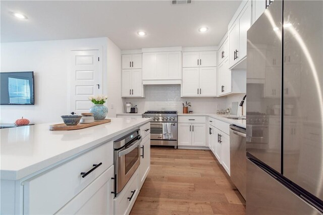 kitchen featuring stainless steel appliances, a sink, light wood-style floors, light countertops, and decorative backsplash