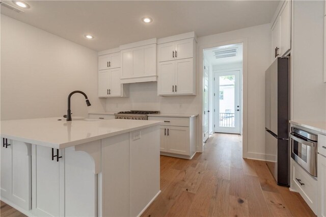 kitchen with light wood-style flooring, oven, a sink, white cabinets, and freestanding refrigerator