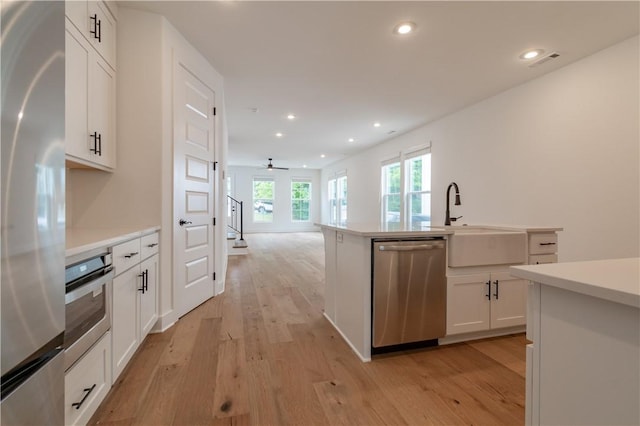 kitchen with stainless steel appliances, recessed lighting, light wood-style floors, white cabinetry, and a sink