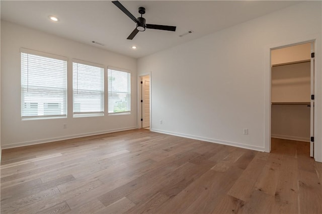 unfurnished bedroom featuring light wood-type flooring, a spacious closet, and baseboards