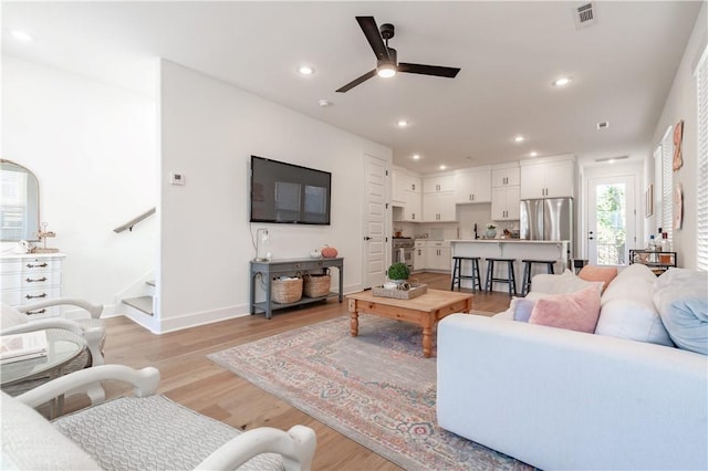 living area featuring light wood finished floors, recessed lighting, visible vents, stairway, and baseboards