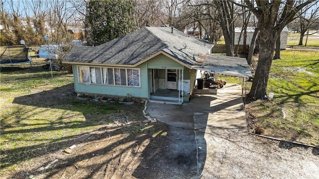 bungalow-style home with driveway, a shingled roof, a trampoline, and a front lawn