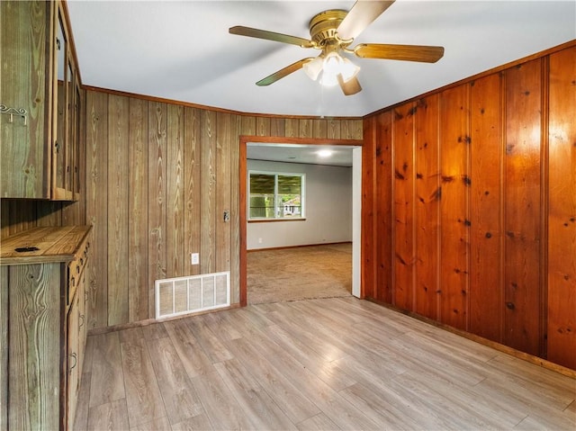 empty room with wooden walls, light wood-style flooring, a ceiling fan, baseboards, and visible vents