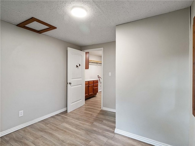 unfurnished room with baseboards, attic access, and light wood finished floors