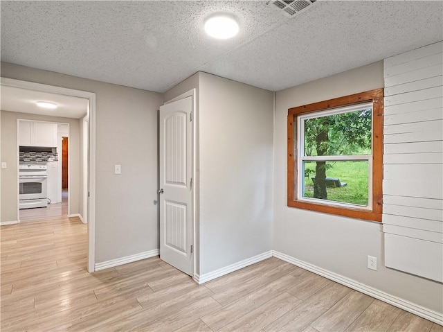 interior space with baseboards, light wood finished floors, a textured ceiling, and visible vents