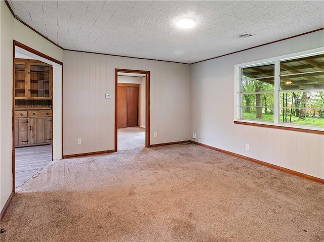 empty room featuring crown molding, baseboards, carpet, and visible vents