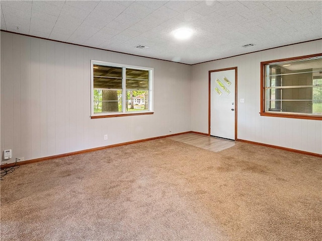 carpeted empty room featuring visible vents, baseboards, and wooden walls