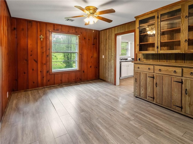 interior space featuring ceiling fan, a sink, light wood-style floors, wood walls, and visible vents