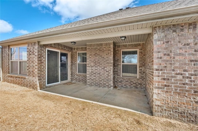 back of house with brick siding, a shingled roof, and a patio