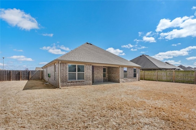 rear view of property with brick siding, a fenced backyard, and roof with shingles