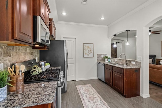 kitchen with appliances with stainless steel finishes, a sink, a ceiling fan, arched walkways, and ornamental molding