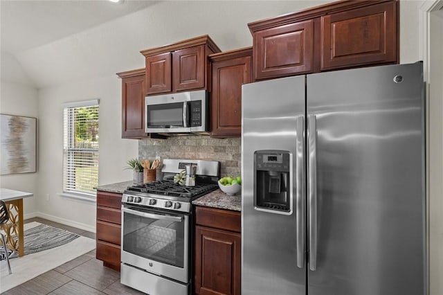 kitchen featuring stainless steel appliances, vaulted ceiling, stone counters, tasteful backsplash, and baseboards