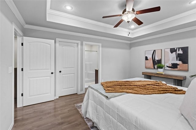 bedroom featuring a tray ceiling, wood finished floors, crown molding, ensuite bathroom, and recessed lighting