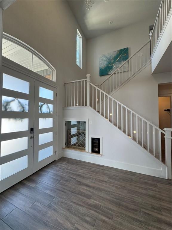 unfurnished living room featuring baseboards, a towering ceiling, wood finished floors, stairs, and french doors