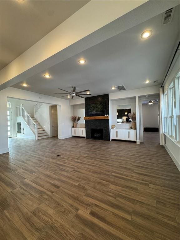 unfurnished living room with a large fireplace, stairway, visible vents, and a ceiling fan