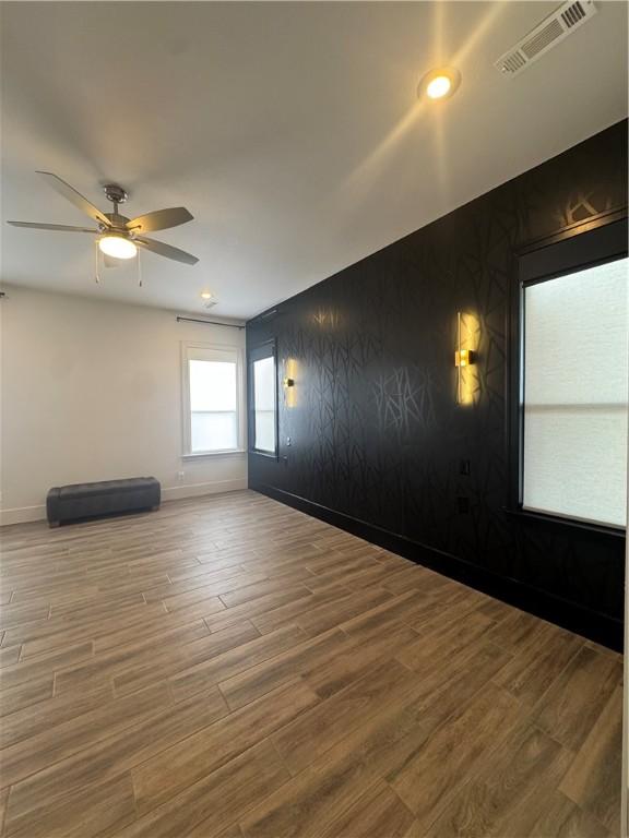 empty room featuring ceiling fan, wood finished floors, visible vents, and baseboards