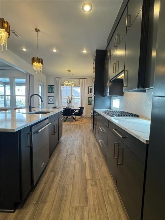 kitchen featuring dark cabinets, stainless steel appliances, wood finish floors, a chandelier, and a sink