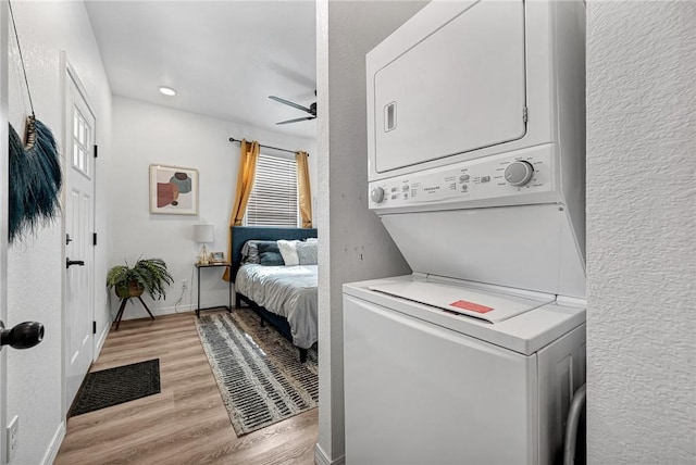 washroom with stacked washer and dryer, a ceiling fan, light wood finished floors, baseboards, and laundry area