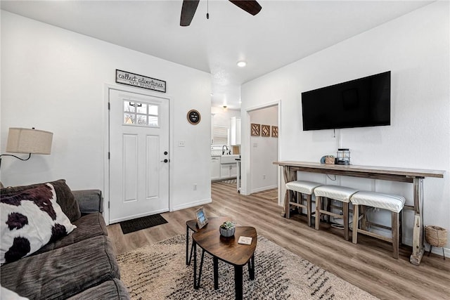 living area with baseboards, light wood-type flooring, and ceiling fan