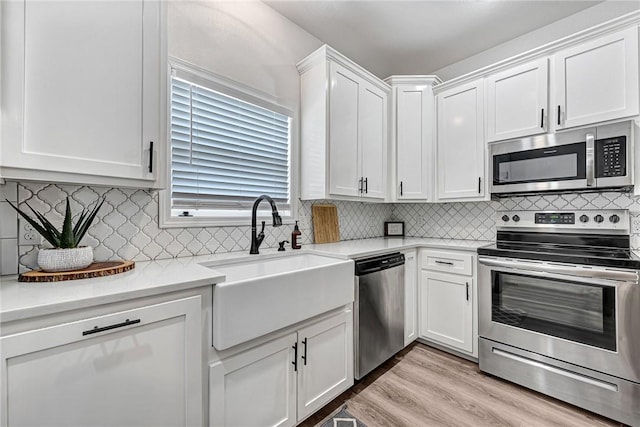 kitchen featuring light wood-type flooring, light countertops, appliances with stainless steel finishes, white cabinets, and a sink