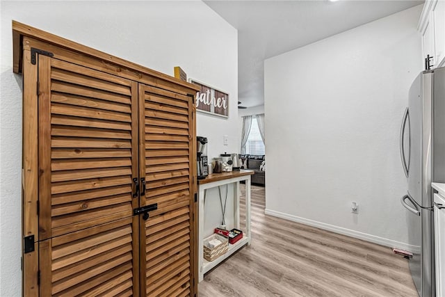 interior space with white cabinetry, freestanding refrigerator, baseboards, and light wood finished floors