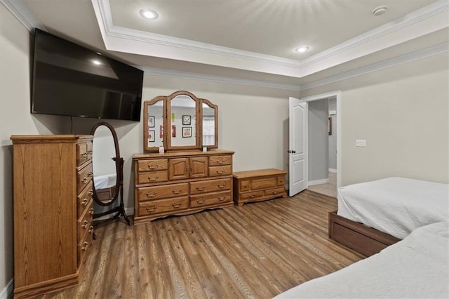 bedroom with baseboards, ornamental molding, a raised ceiling, and wood finished floors