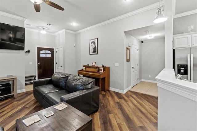 living room featuring baseboards, visible vents, a ceiling fan, ornamental molding, and wood finished floors