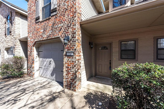 doorway to property featuring brick siding, driveway, and an attached garage