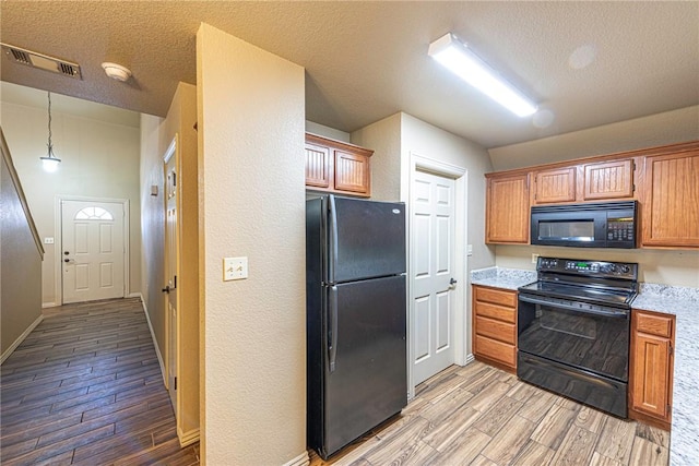 kitchen featuring light countertops, visible vents, a textured ceiling, light wood-type flooring, and black appliances