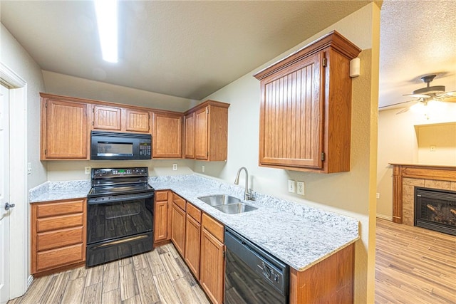 kitchen with black appliances, light wood finished floors, a tiled fireplace, and a sink