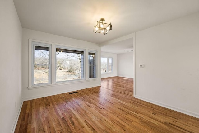 empty room featuring an inviting chandelier, wood finished floors, visible vents, and baseboards