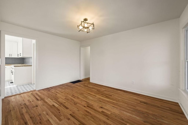 spare room with an inviting chandelier, visible vents, baseboards, and wood finished floors