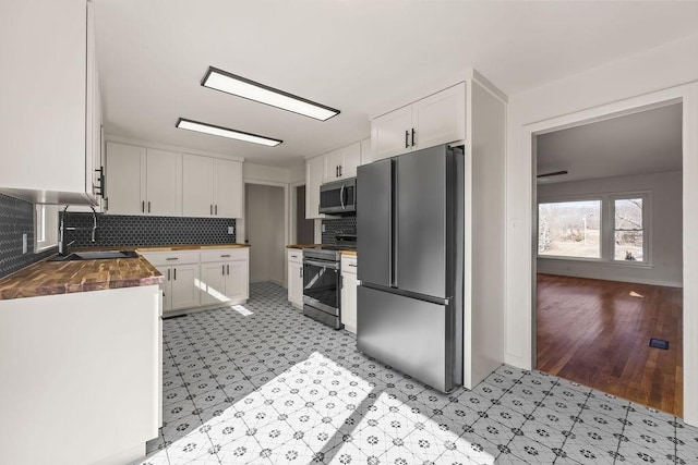 kitchen with stainless steel appliances, tasteful backsplash, white cabinets, a sink, and butcher block countertops