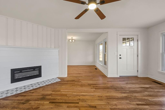 entrance foyer with a glass covered fireplace, visible vents, baseboards, and wood finished floors