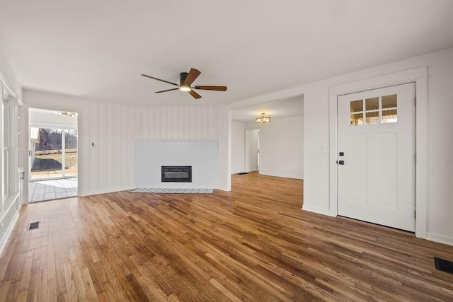 unfurnished living room with a glass covered fireplace, visible vents, ceiling fan, and wood finished floors